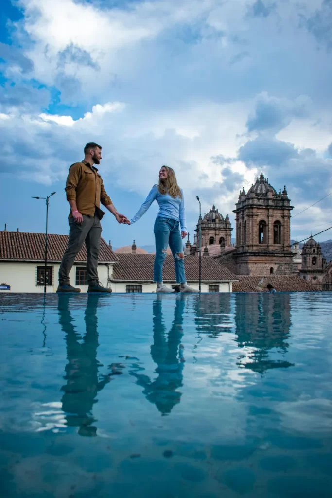 couple rainy day cusco main square peru honeymoon weather A happy couple taking a photo at Cusco’s Plaza de Armas after the rain, enjoying the charm of Peru honeymoon weather.
